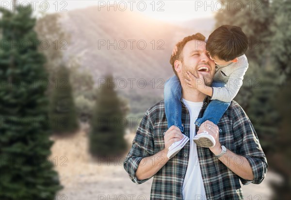 Happy mixed-race chinese boy riding piggyback on shoulders of caucasian father at christmas tree farm