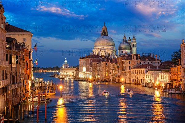 View of Venice Grand Canal with boats and Santa Maria della Salute church in the evening from Ponte dell'Accademia bridge. Venice