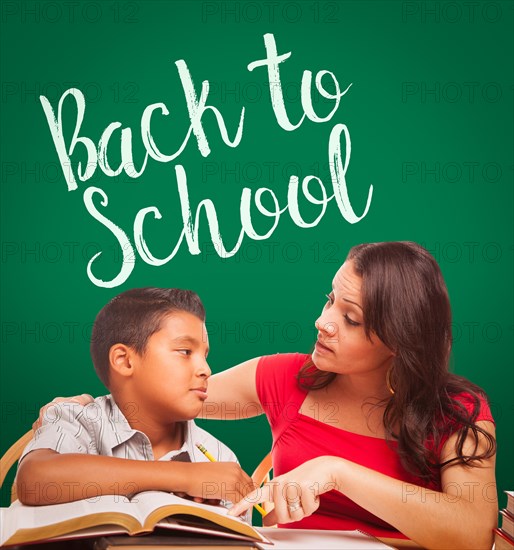 Back to school written on chalk board behind hispanic young boy and famale adult studying