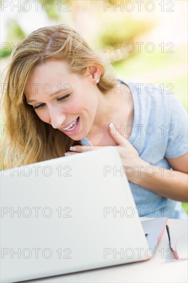 Young adult woman live video chatting outdoors using her laptop