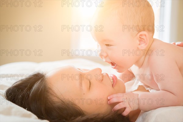 Young mixed-race chinese and caucasian baby boy laying in his bed with his mother