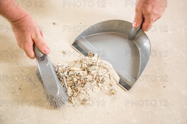 Worker picking up pile of debris on cement with brush and dust pan