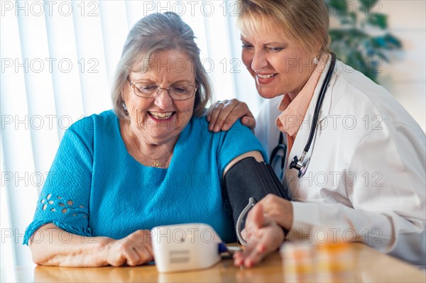 Senior adult woman learning from female doctor to use blood pressure machine