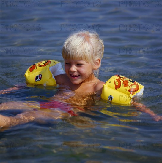 Little girl with water wings practices backstroke