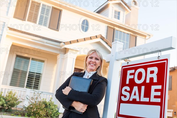 Female real estate agent in front of for sale sign and beautiful house