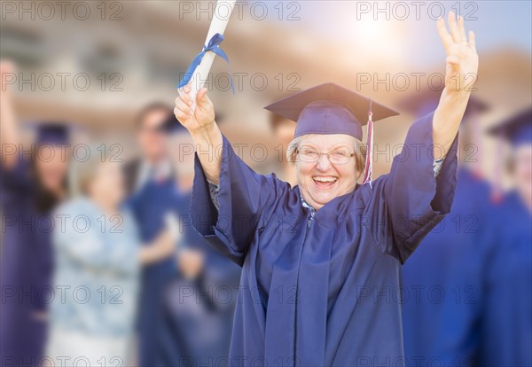 Happy senior woman in hat and gown at outdoor graduation ceremony