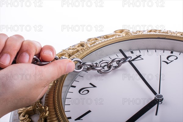 Chain tied to minute hand of a clock and pulled on a white background