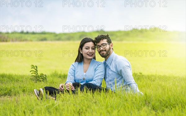 Young couple in love sitting on the grass looking at the camera