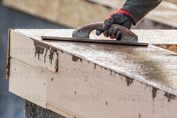 Construction worker using wood trowel on wet cement forming coping around new pool