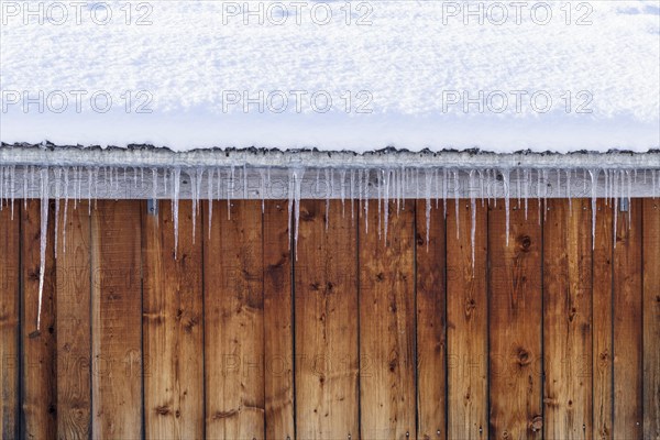Icicles on the roof in front of a wooden wall
