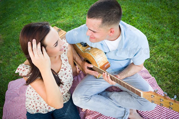 Young adult man playing guitar for his girlfriend in the park