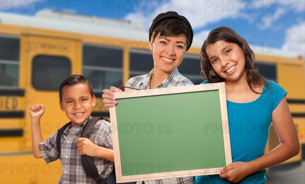 Young mixed-race students with blank chalkboard near school bus