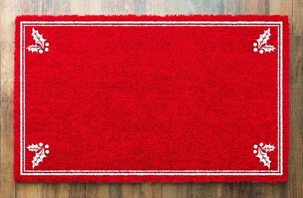 Blank holiday red welcome mat with holly corners on wood floor ...