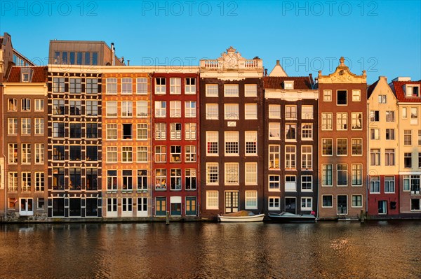 Houses and tourist boats on Amsterdam canal pier Damrak on sunset. Amsterdam
