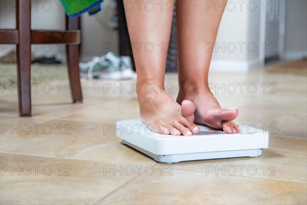 Woman standing on scale at home reluctantly viewing weight