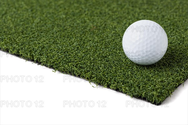 Golf ball resting on section of artificial turf grass on white background