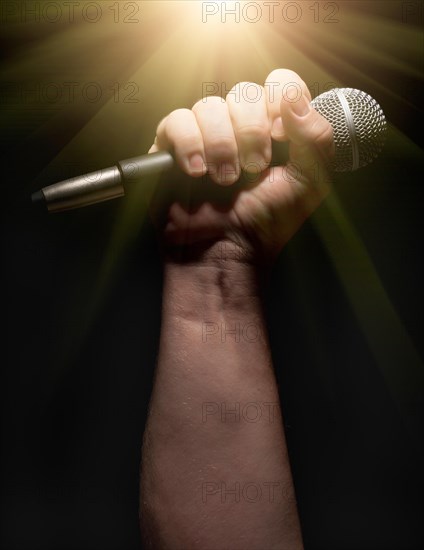 Vertical microphone clinched firmly in male fist on a black background