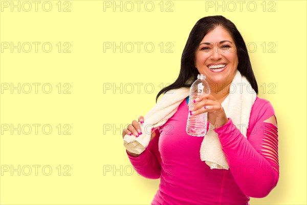 Middle aged hispanic woman in workout clothes with towel and water bottle against A bright yellow background