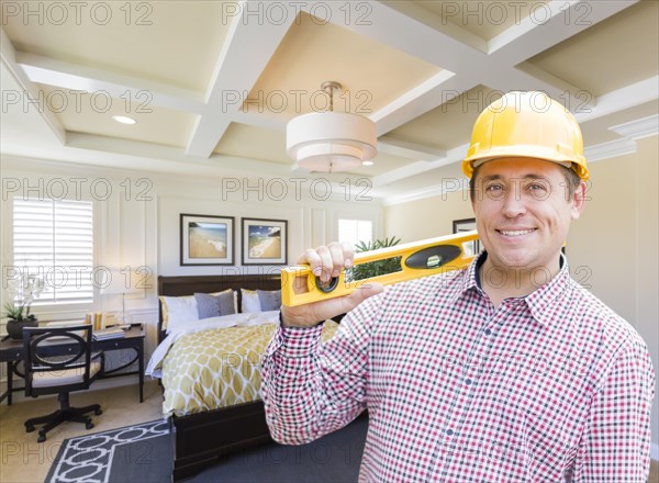 Smiling contractor in hard hat with level over custom bedroom drawing and photo combination