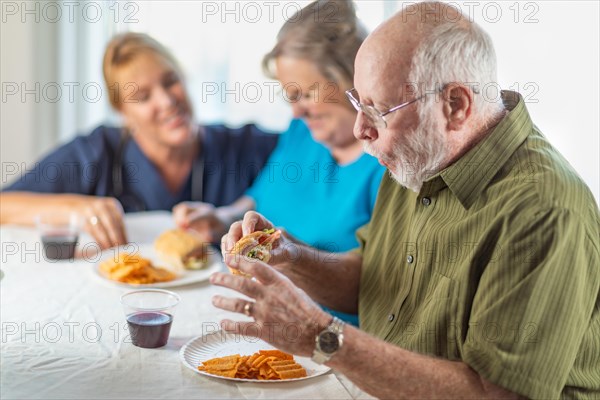 Female doctor or nurse serving senior adult couple sandwiches at table