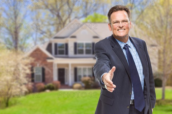 Smiling male agent reaching for hand shake in front of beautiful new house