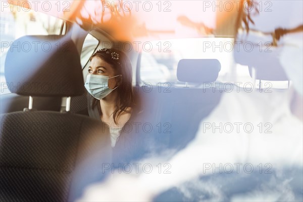 A woman wearing a protective mask sitting on the back seat of a taxi car