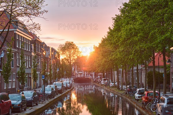 Delt canal with old houses and cars parked along on sunset. Delft