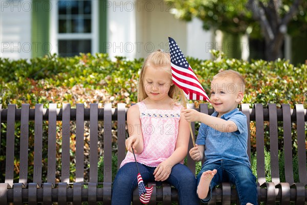 Young sister and brother comparing each others american flag size on the bench at the park