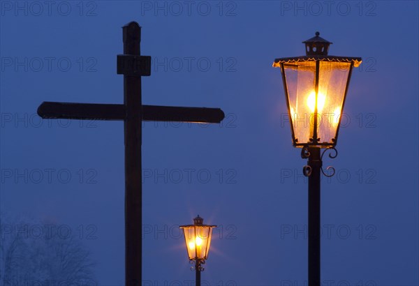 Holzkreuz mit Strassenlaternen in der Abenddaemmerung