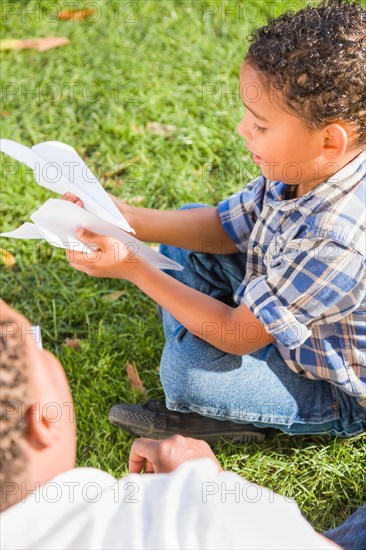 Happy african american father and mixed-race son playing with paper airplanes in the park