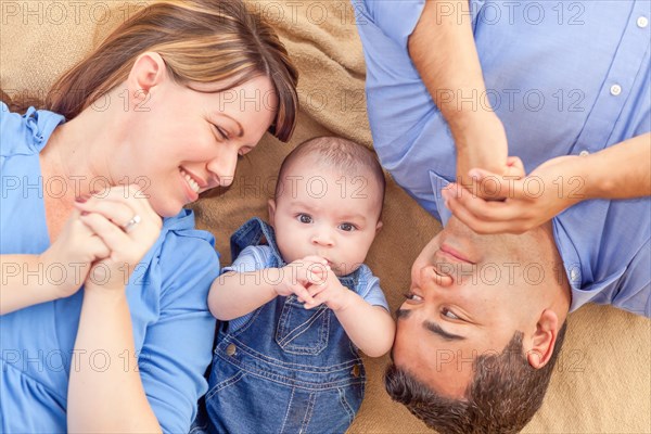 Young mixed-race couple laying with their infant on A blanket