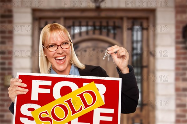 Excited woman holding house keys and sold real estate sign in front of nice new home