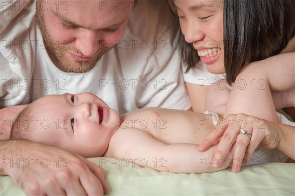 mixed-race chinese and caucasian baby boy laying in bed with his father and mother