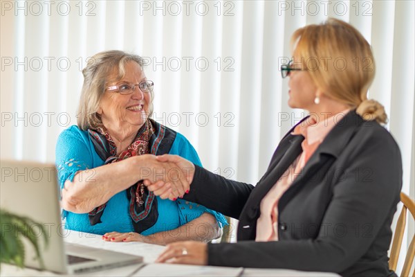 Senoir woman shaking hands with businesswoman near laptop computer