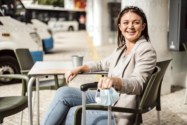 A young traveler with the luggage and protective mask sitting in the cafe and waiting for her bus to come