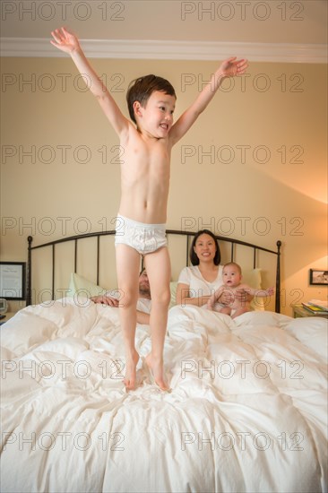 Young mixed-race chinese and caucasian boy jumping in bed with his family