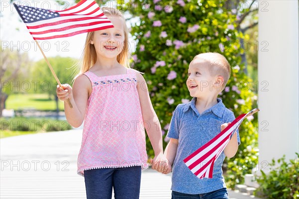 Young sister and brother waving american flags at the park