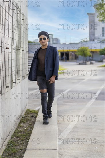 Latin gay male with makeup wearing fashion hat doing catwalk in the street