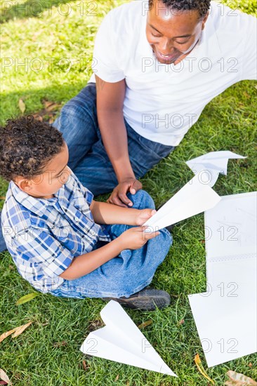 Happy african american father and mixed-race son playing with paper airplanes in the park