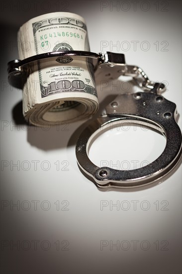 Handcuffs locked on roll of one hundred dollar bills under spotlight