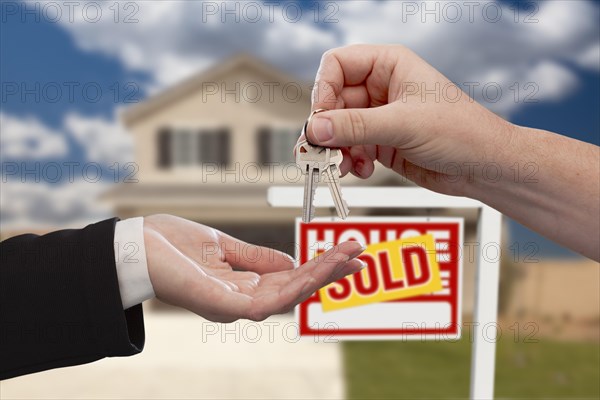 Handing over the house keys in front of real estate sign and sold new home