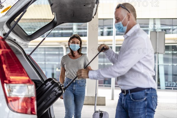 A taxi or Uber driver helping a passenger in a protective mask with her luggage at the airport