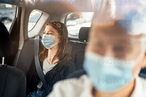 A woman wearing a protective mask sitting on the back seat of a taxi car