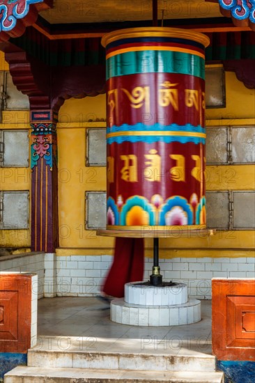 Buddhist monk rotating big prayer wheel with Om Mani Padme Hum Buddhist mantra prayer meaning Praise to the Jewel in the Lotus on kora around Tsuglagkhang complex. McLeod Ganj