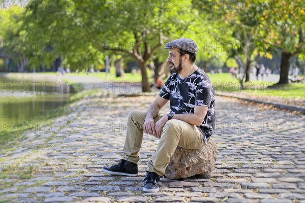 Mature man sitting on a tree trunk looking pensively at a lake. Copy space