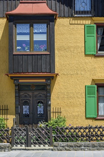 Yellow wooden shingle facade with bay window and green shutters