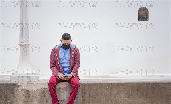 Guy with surgical mask sitting in with his cell phone