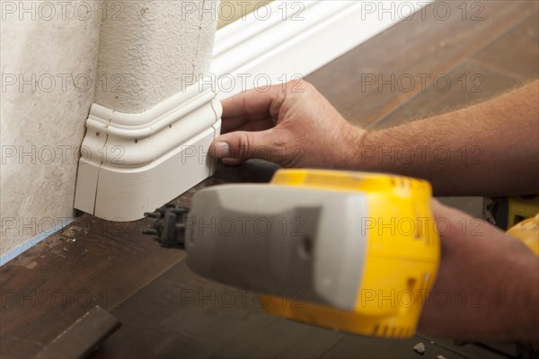 Contractor nailing new baseboard with bull nose corners and new laminate flooring renovation abstract