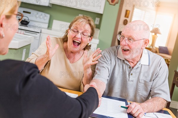 Senior adult couple celebrating over documents in their home with agent at signing