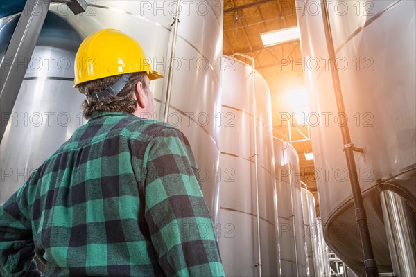 Man wearing hard hat looking up at large industrial tanks